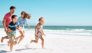 Cheerful young family running on the beach with copy space. Happy mother and smiling father with two children, son and daughter, having fun during summer holiday. Playful casual family enjoying playing at beach during vacation.