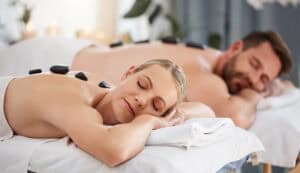 Couple, relax and stone massage in spa for wellness, zen vacation and body pain. Man, woman and hot rock treatment in luxury salon for healing muscle, physical therapy and calm holiday in Thailand.